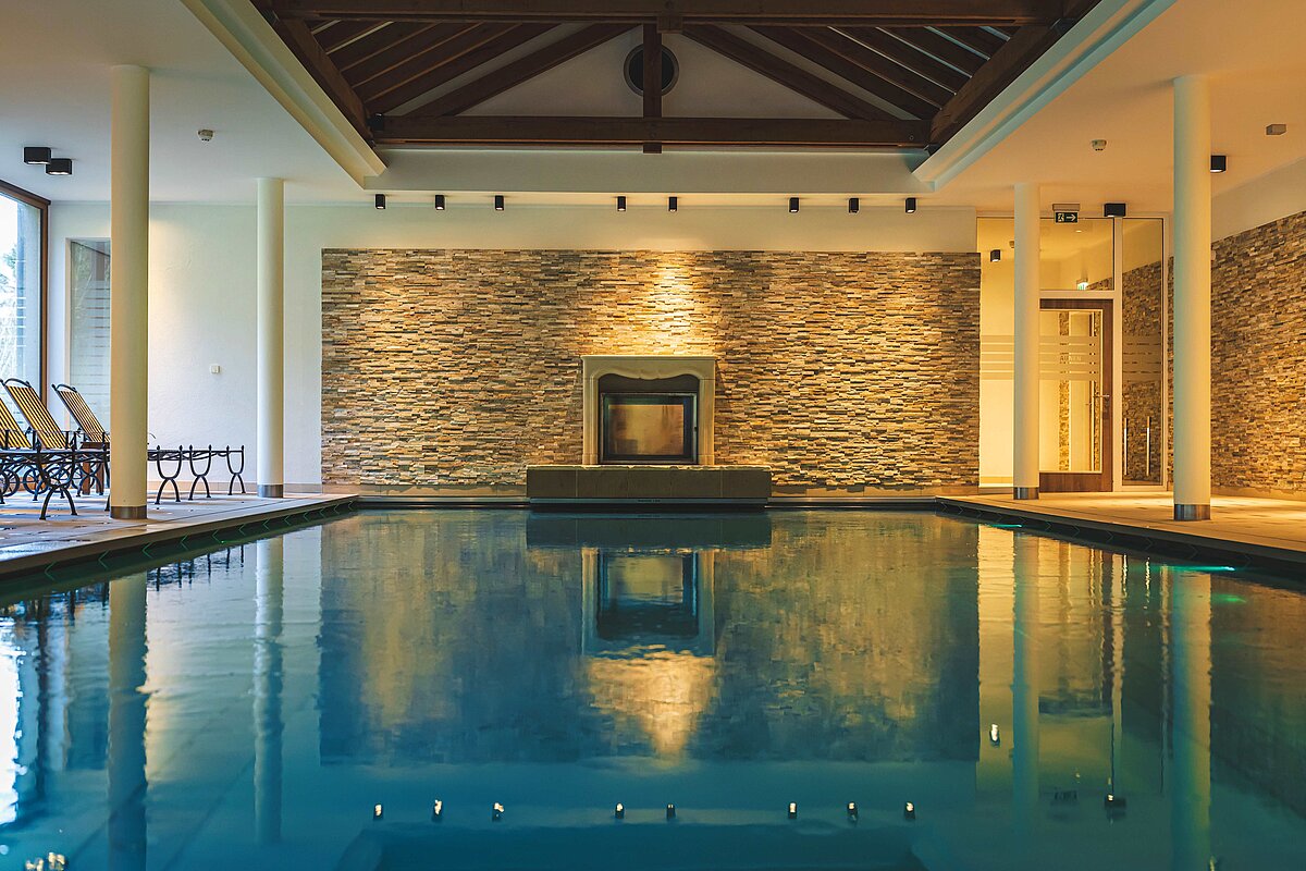 Blick auf den Pool mit Steinwand und Kamin im Hintergrund