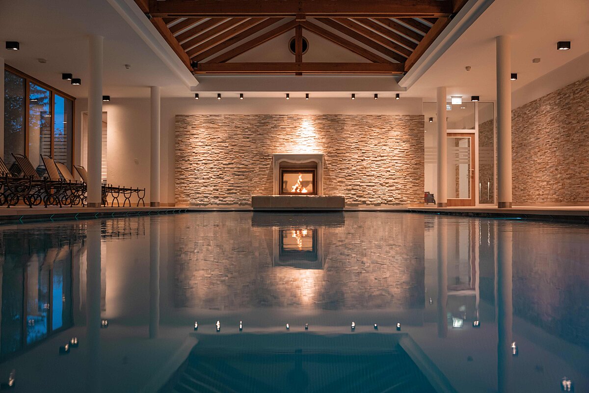 Blick vom Pool auf Steinwand mit Kamin am Abend