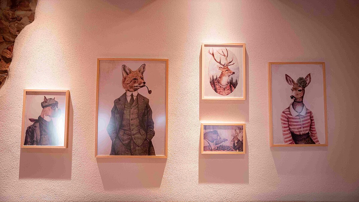 Blick auf Steinwand mit fünf Bilderrahmen die Wladtiere zeigen, welche menschenkleidung tragen.