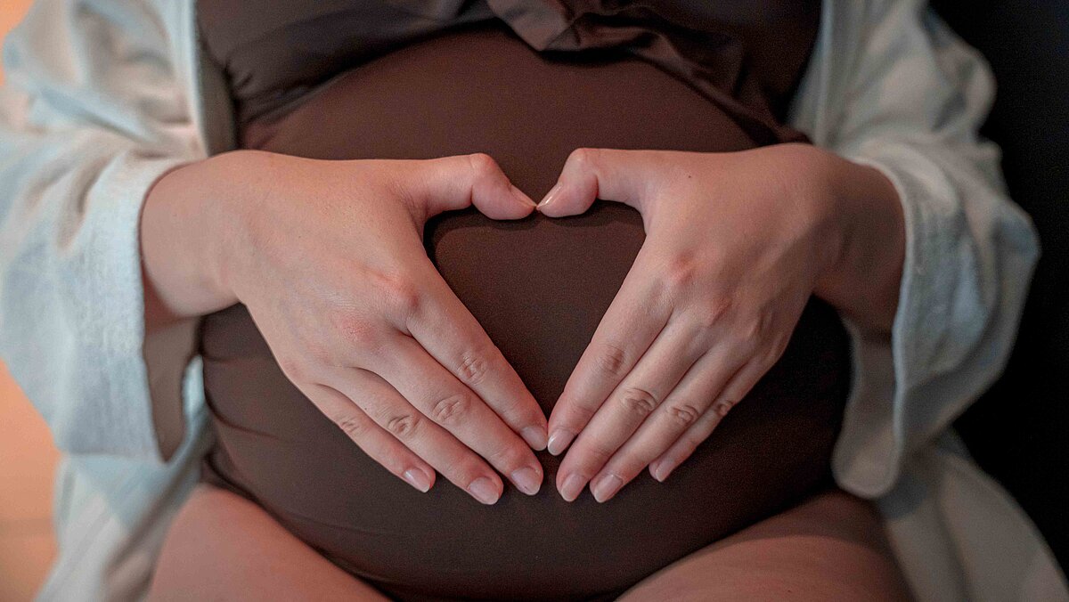 Bild den Babybuch einer Frau die ihre Haende auf dem Bauch zu einem herzen formt.